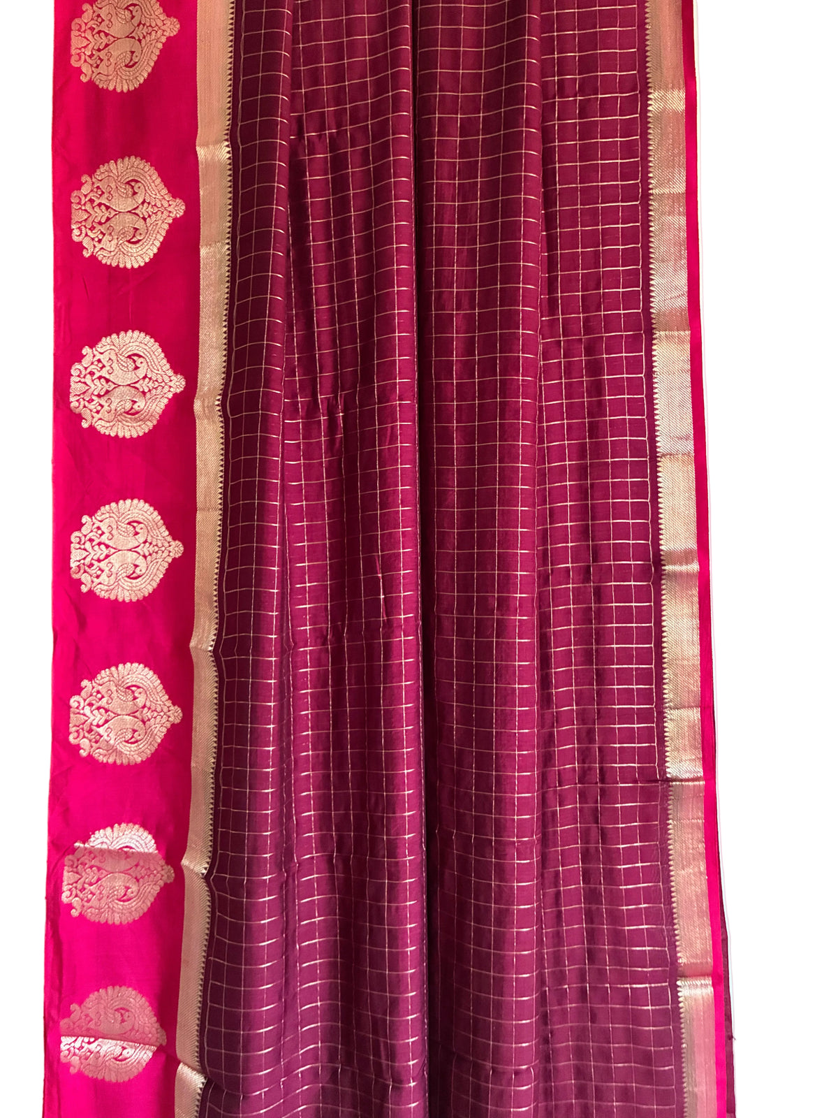 A close-up of a traditional Indian saree fabric, showing a deep magenta body with a fine white grid pattern and a contrasting bright pink border adorned with gold zari motifs. aariyaa sarees for festive wear 