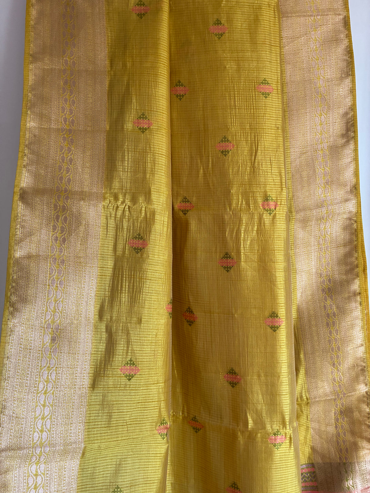 Close up of soft breathable yellow fabric with delicate multicolour butta weave and antique gold border