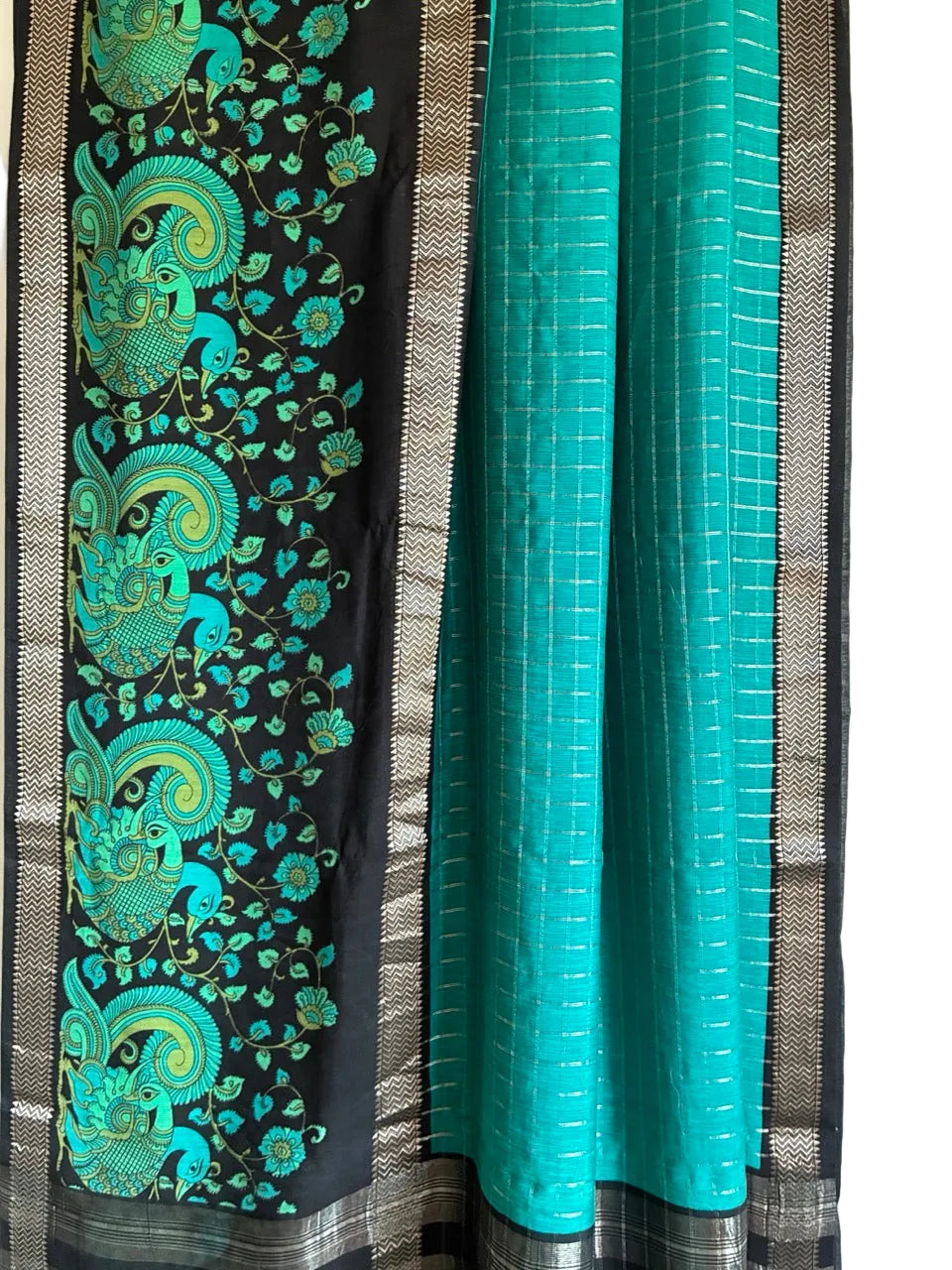 Close up of soft breathable teal blue saree fabric featuring intricate Kalamkari motifs and black accents